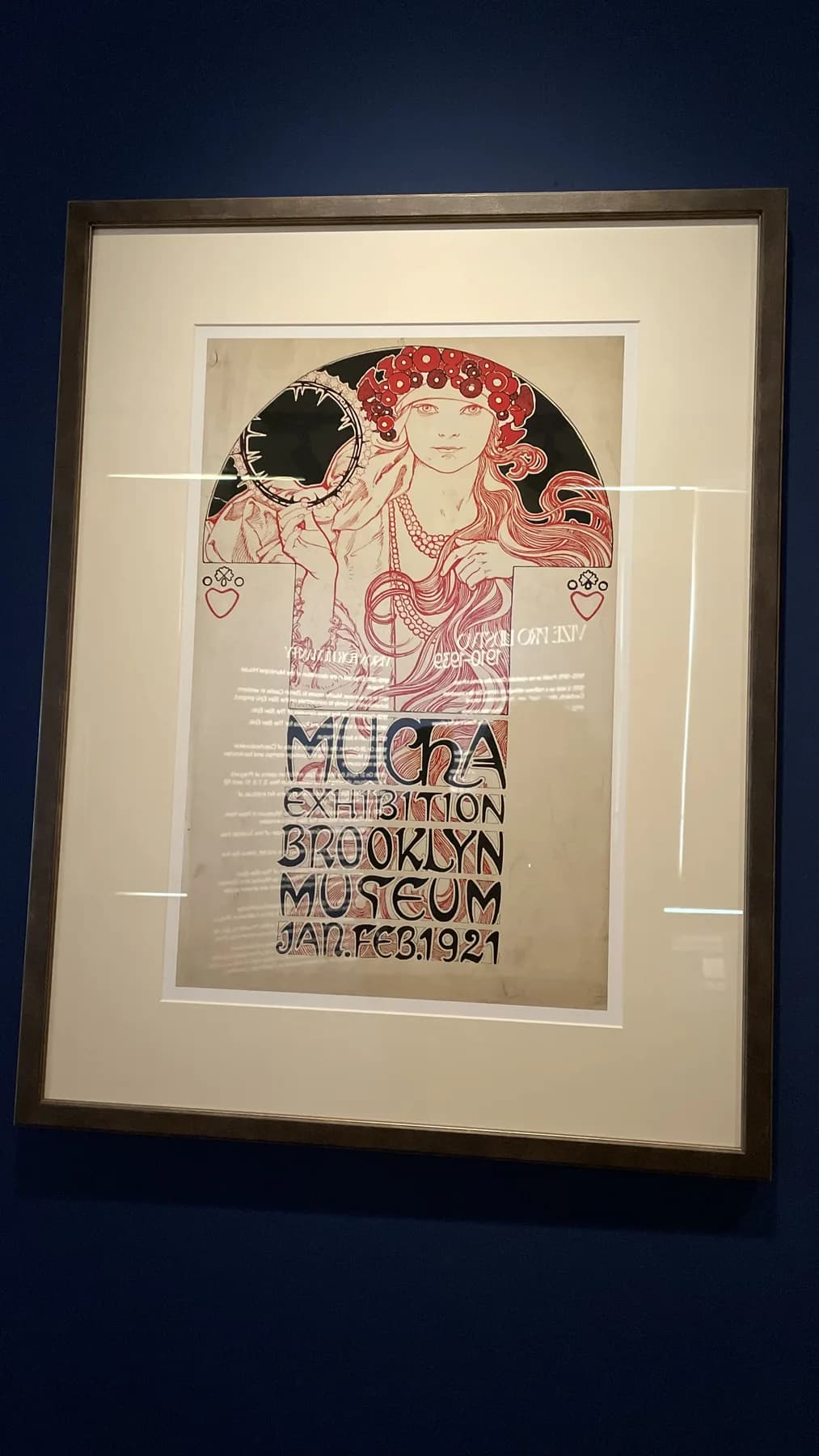 A framed 1921 Brooklyn Museum exhibition poster for Mucha, using a Mucha-style figure and bold exhibition lettering.